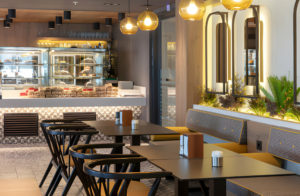 Modern cafe interior with black chairs, yellow booths, and a display case of pastries.
