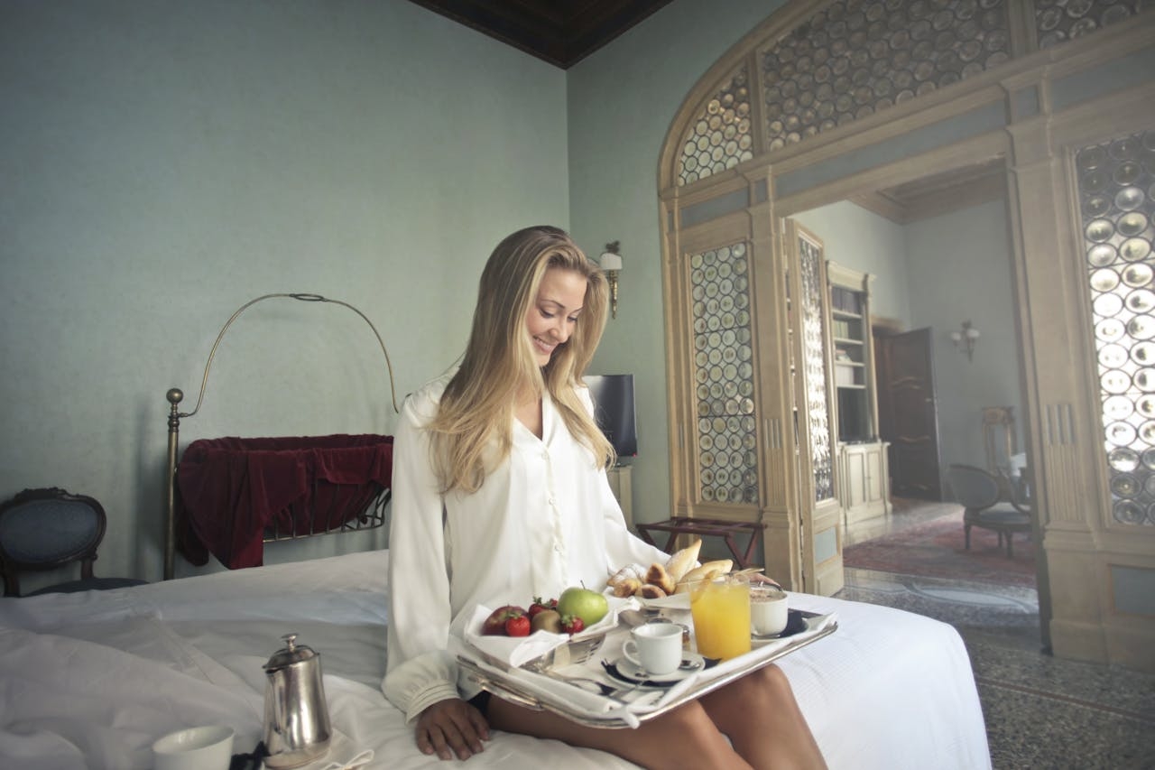 Cheerful woman with breakfast on tray in hotel bedroom