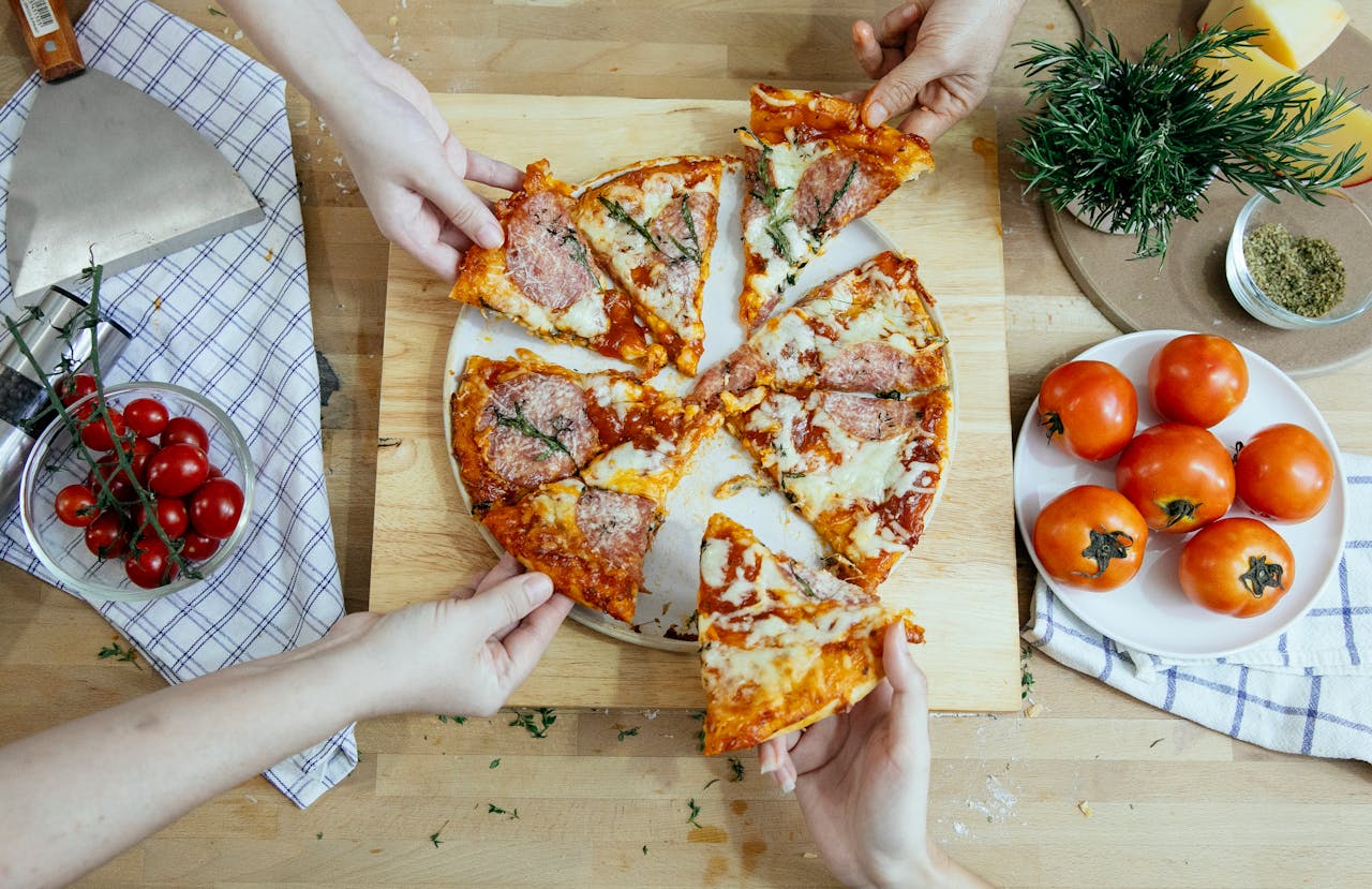 friends taking slices of delicious pizza from cutting board