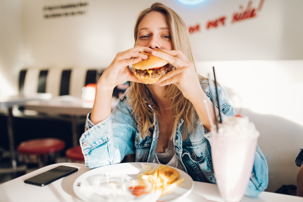 young woman eating burger and milkshake
