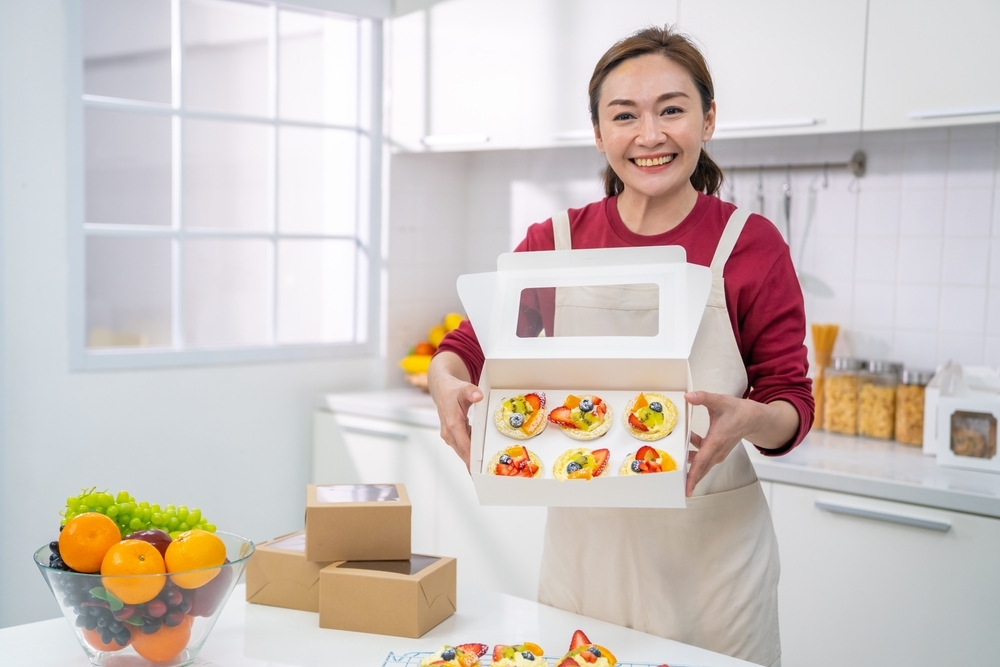 asian woman in her home bakery showing off cupcakes