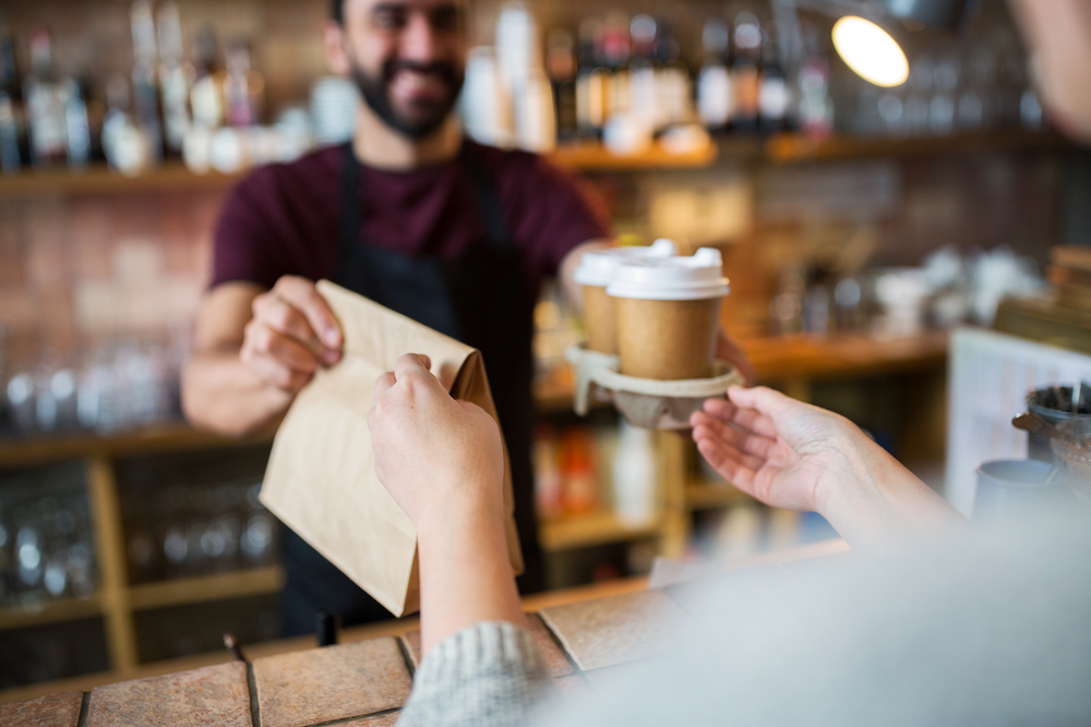 coffee shop manager serving customer coffee with paper bag and paper cup