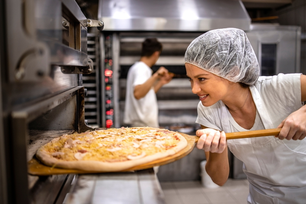 female chef putting pizza in an oven