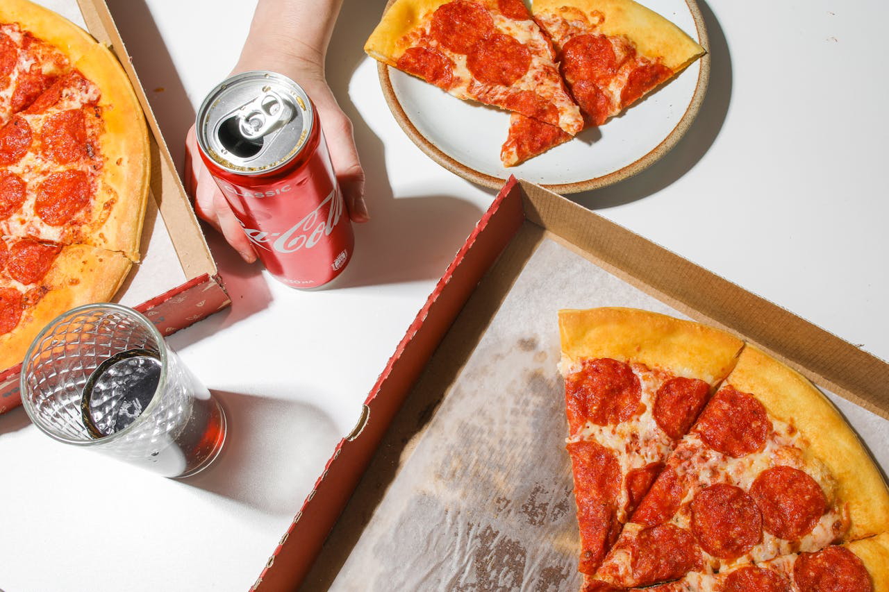 Person Holding Coca Cola In Can Beside Pizza on Table