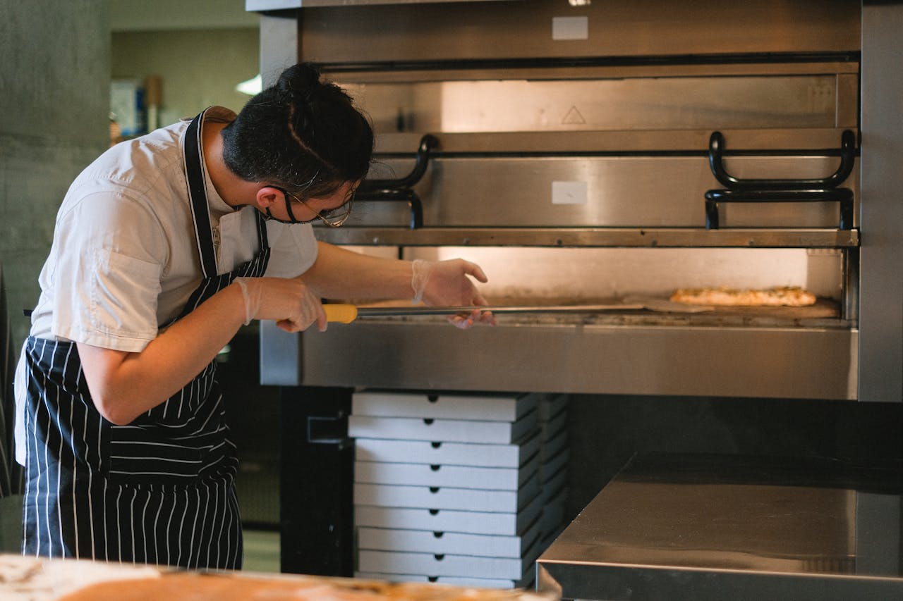 A Man Putting a Pizza in the Oven with a Pizza Peel