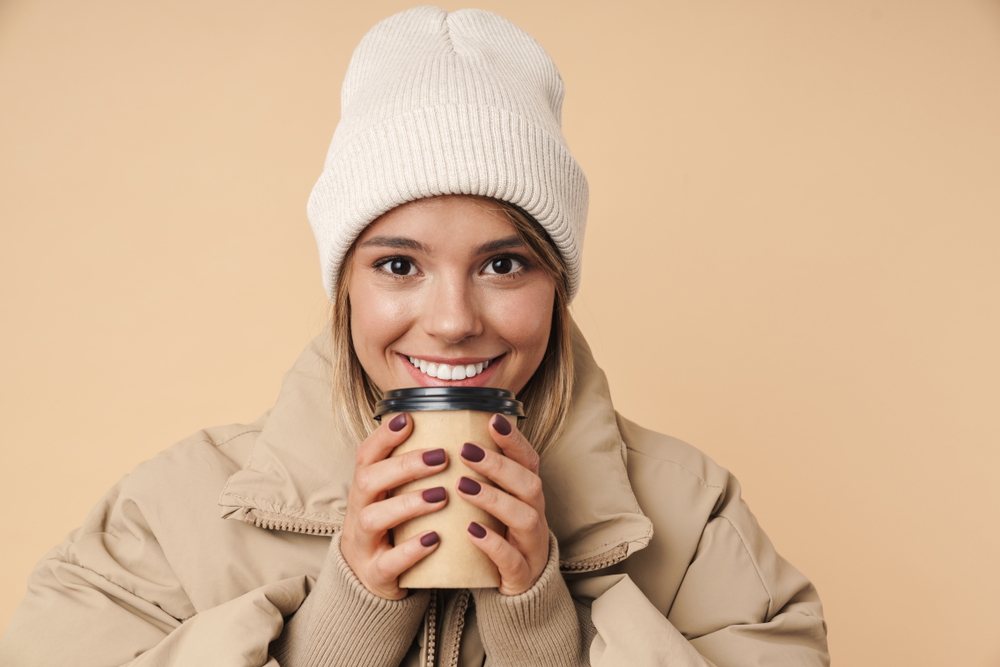 smiling young woman winter coat drinking cup of coffee