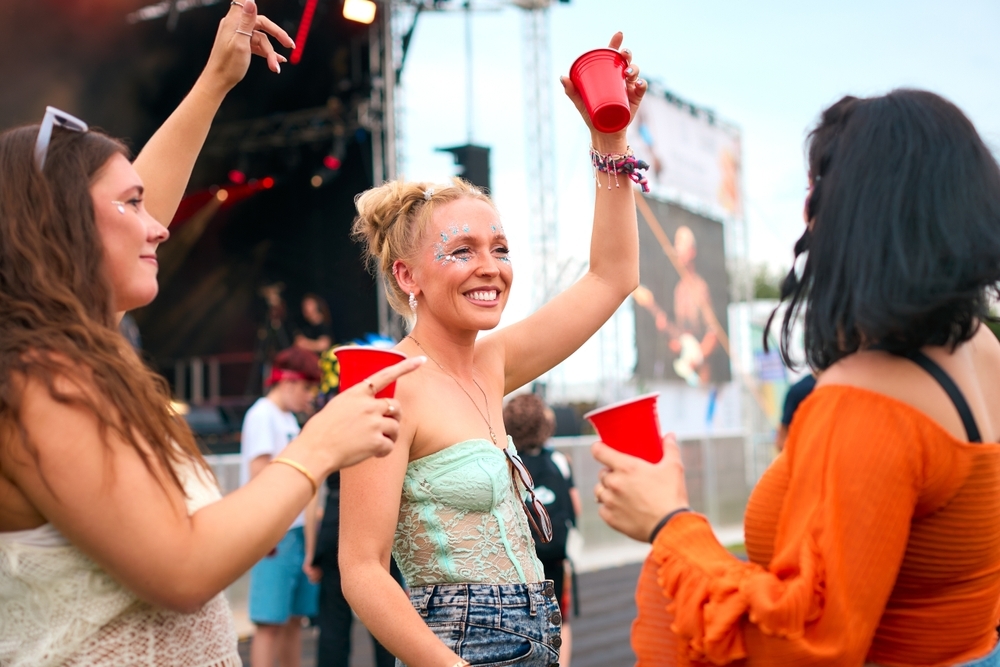 three female friends at a music event holding paper cups
