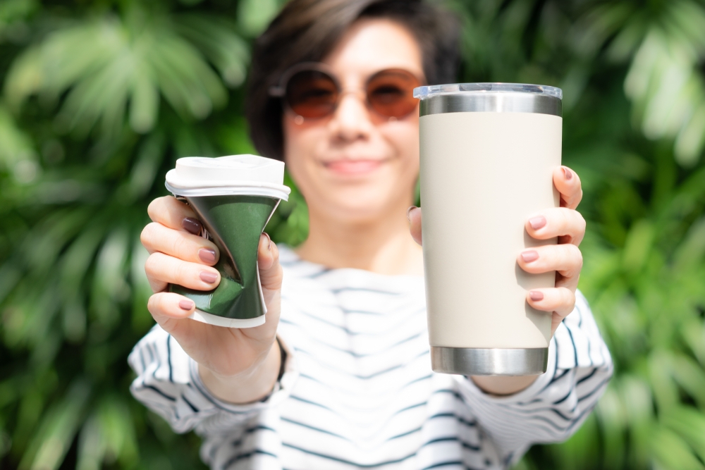 woman holding reusable takeaway coffee cup and paper cup